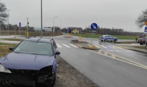 Rozbity przód pojazdu ford mondeo koloru granatowego, w tle radiowóz policyjny z włączonymi sygnałami świetlnymi