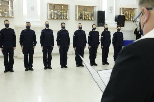 Ksiądz Bogdan Zagórski błogosławi nowych funkcjonariuszy policji. W drugim planie zdjęcia w szeregu obok siebie stoją w granatowych mundurach młodzi policjanci.