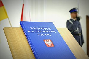 W pierwszym planie zdjęcia Konstytucja Rzeczypospolitej Polskiej w drugim planie niewyraźna sylwetka dowódcy uroczystości.