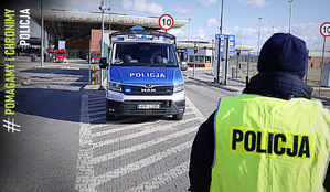 W pierwszym planie zdjęcia stoi policjant na przejściu granicznym Dołhobyczowie. W drugim planie zdjęcia radiowóz oznakowany z napisem policja.