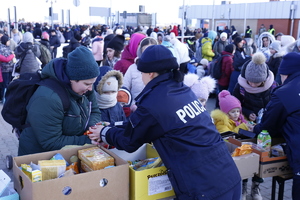 Policjantka przekazuje żywność uchodźcom.