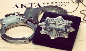 Kajdanki policyjne, odznaka z napisem policja oraz akta sprawy.