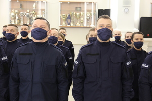 W pierwszym planie zdjęcia policjanci ubrani w granatowy mundur z napisem policja oraz z założonymi maseczkami ochronnymi zakrywającymi usta i nos.