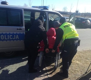 policjanci pomagaj wsiąść do radiowozu osobie na wózku inwalidzkim