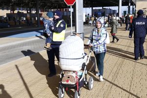 policjant trzyma na ręku małe dziecko, obok stoi matka z wózkiem