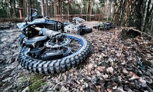 leżący na leśnej drodze uszkodzony motocykl marki Yamaha, w tle metalowy szlaban i policyjny radiowóz