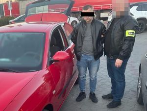 zatrzymany oszust i policjant stoją przy czerwonym aucie