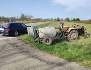na poboczu drogi stoi ciągnik rolniczy z opryskiwaczem. obok niego stoi granatowy samochód BMW