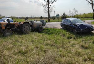 na poboczu drogi stoi ciągnik rolniczy z podpiętym opryskiwaczem oraz obok niego niebieski samochód BMW z rozbitym przodem