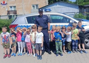 zdjęcie grupowe policjant z grupą dzieci z przedszkola na tle radiowozu