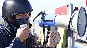 Zdjęcie przedstawia policyjnego negocjatora w kasku ochronny z megafonem w ręku.