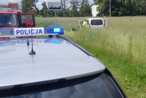 miejsce wypadku drogowego, radiowóz, stojący w polu uszkodzony pojazd, obok policjant