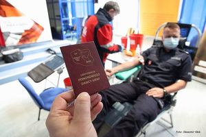 legitymacja honorowego dawcy krwi. W tle policjant oddający krew