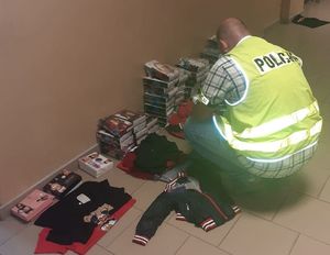 policjant i leżąca na podłodze zabezpieczona odzież z podrobionymi znakami towarowymi