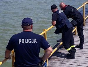 policjant i strażacy na pomoście, w tle widać zbiornik wodny