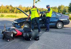 zdjęcie przedstawia policjantów stojących przy motocyklu i samochodzie który brał udział w zdarzeniu drogowym