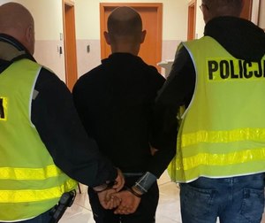 policjanci w odblaskowych kamizelkach prowadzą zatrzymanego mężczyznę