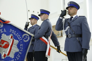 Zdjęcie przedstawia funkcjonariuszy pocztu sztandarowego.  Dwóch funkcjonariuszy oddaje honor a jeden trzyma sztandar.