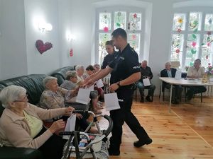 policjant przekazuje seniorom ulotki