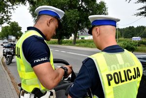 dwóch policjantów kontroluje pojazd. W tle motocykl policyjny