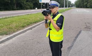 policjantka z drogówki stoi na drodze z miernikiem prędkości