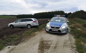 Zabezpieczony samochód marki Opel, który wjechał na pole. Po prawej stronie oznakowany samochód policyjny.