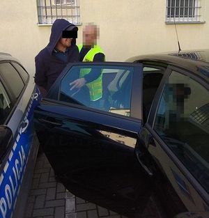 zatrzymany mężczyzna wsiada do samochodu, obok policjant