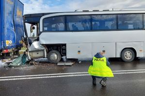 Uszkodzony samochód ciężarowy, a za nim uszkodzony autobus oraz policjant
