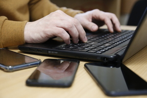 dłonie mężczyzny na klawiaturze laptopa. obok trzy telefony komórkowe