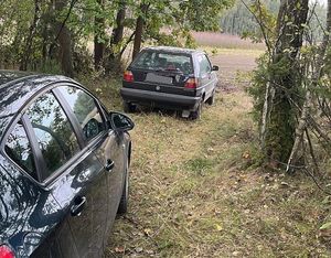 skradziony samochód zaparkowany na leśnej ścieżce. Za nim fragment nieoznakowanego radiowozu