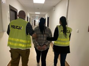 Policjanci prowadzą zatrzymaną kobietę.
