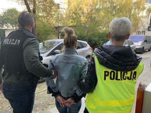 Policjanci prowadzą zatrzymaną kobietę.