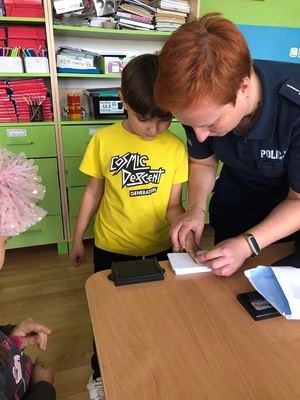 policjantka pokazuje dziecku w jaki sposób zabezpiecza się odbitki linii papilarnych