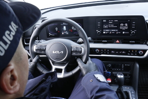 Policjant ubrany w mundur z napisami policja siedzi za kierownicą nowego radiowozu marki Kia Sportage.