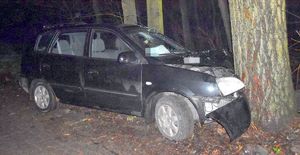 Samochód marki Kia z uszkodzeniami przedniej części stoi przy drzewie