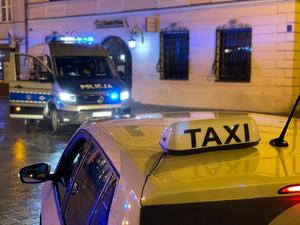 W pierwszym planie zdjęcia napis taxi na dachu samochodu osobowego w drugim planie zdjęcia widzimy oznakowany radiowóz policji.