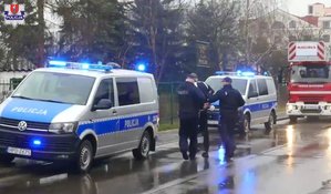 policjanci prowadzą mężczyznę w kajdankach przez ulicę, obok radiowóz