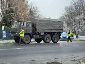 Pojazd wojskowy i radiowóz na ulicy. W tle policjant i wojskowy