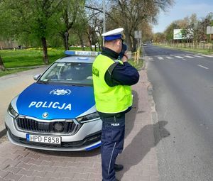 policjant drogówki z miernikiem prędkości przy drodze. Obok radiowóz