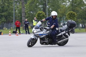 Funkcjonariusz na motocyklu omija pachołki ustawione na placu.