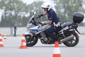 Funkcjonariusz na motocyklu omija pachołki ustawione na placu.
