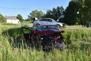 rozbity pojazd w trawie, za nim srebrne auto