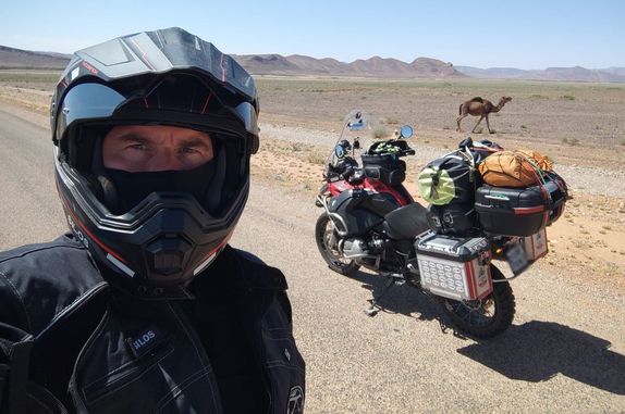 motocyklista na tle pustyni i wielbłąda