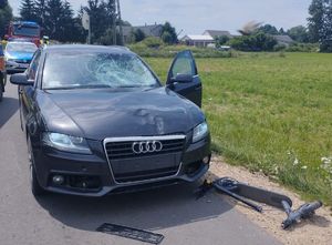 uszkodzony samochód marki Audi, leżąca na drodze hulajnoga, w tle policjant