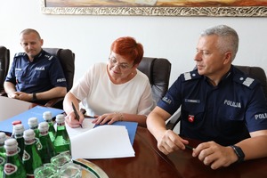 za stołem siedzą trzy osoby i podpisują dokument: Starostwa Lubartowski, dyrektor szkoły w Kocku oraz komendant wojewódzki Policji w Lublinie