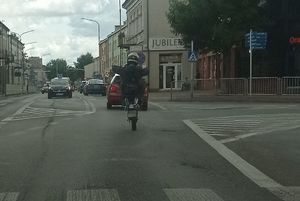 motocyklista jadący na jednym kole, w tle skrzyżowanie z sygnalizacją świetlną