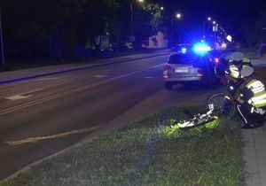 Oznakowany radiowóz oraz dwóch policjantów na miejscu zdarzenia drogowego z udziałem rowerzysty.