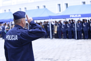 Po lewej stronie zdjęcia policjant umundurowany oddaje honor podczas odgrywanego Hymnu Polski.