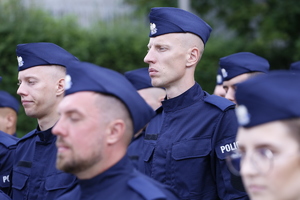 Nowi funkcjonariusze ubrani w granatowe mundury z napisami policja. Na głowie policjanci mają założone furażerki.