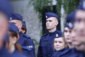 Nowi funkcjonariusze ubrani w granatowe mundury z napisami policja. Na głowie policjanci mają założone furażerki.